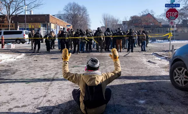 A protester sits on the street with his arms up in front of federal agents in Minneapolis, on Saturday, Jan. 24, 2026. (Alex Kormann/Star Tribune via AP)
