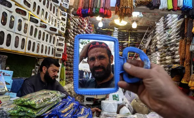 A man tries on a traditional cap which will be used while praying during the Muslim fasting month of Ramadan, at a shop, in Peshawar, Pakistan, Monday, Feb. 16, 2026. (AP Photo/Muhammad Sajjad)