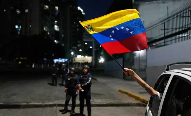 A supporter of the opposition waves a Venezuelan flag from a passing vehicle next to El Helicoide, the headquarters of the intelligence service and a detention center, after several political prisoners were released from custody in Caracas, Venezuela, Sunday, Feb. 8, 2026. (AP Photo/Ariana Cubillos)