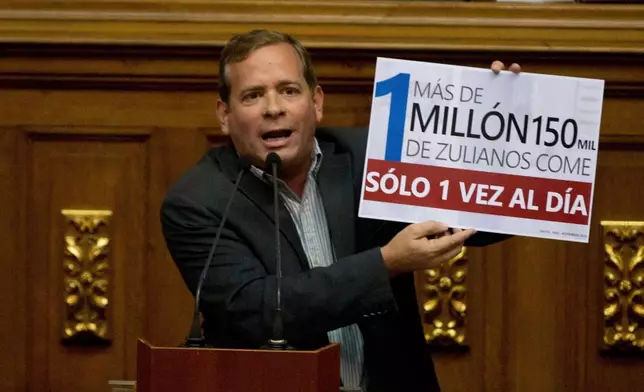 FILE - Opposition lawmaker Juan Pablo Guanipa displays a sign that reads in Spanish "More than a million residents of Zulia State eat only once a day" during an intervention against Venezuela's President Nicolas Maduro at National Assembly, in Caracas, Venezuela, Dec. 13, 2016. (AP Photo/Fernando Llano, File)