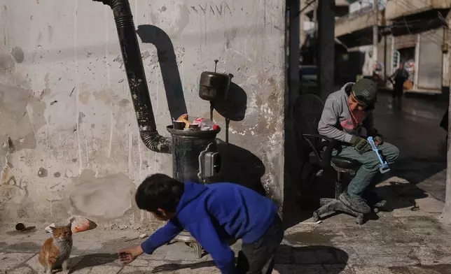 A boy plays with a cat on a street of the Kurdish-majority neighborhood of Sheikh Maqsoud, in Aleppo, Syria, Saturday, Feb. 14, 2026. (AP Photo/Ghaith Alsayed)