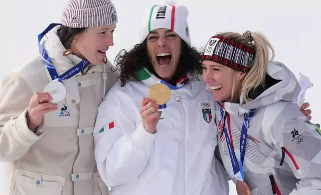 Italy's Federica Brignone, center, gold medalist in an alpine ski, women's super-G race, celebrates with silver medalist France's Romane Miradoli, left, and bronze medalist Austria's Cornelia Huetter, at the 2026 Winter Olympics, in Cortina d'Ampezzo, Italy, Thursday, Feb. 12, 2026. (AP Photo/Jacquelyn Martin)