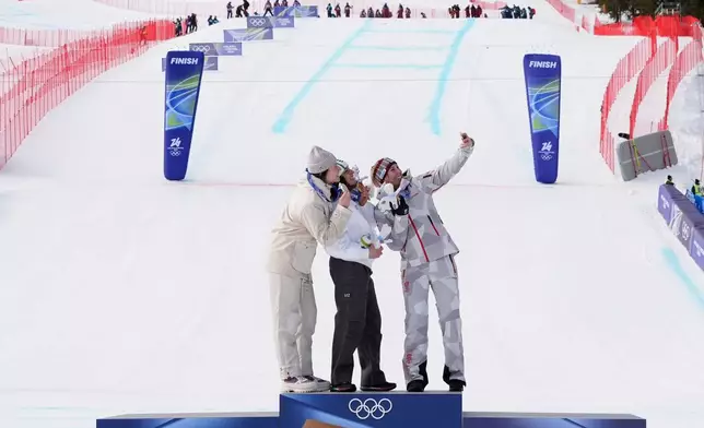 Italy's Federica Brignone, center, gold medalist in an alpine ski, women's super-G race, silver medalist France's Romane Miradoli, left, and bronze medalist Austria's Cornelia Huetter, take a selfie at the 2026 Winter Olympics, in Cortina d'Ampezzo, Italy, Thursday, Feb. 12, 2026. (AP Photo/Jacquelyn Martin)