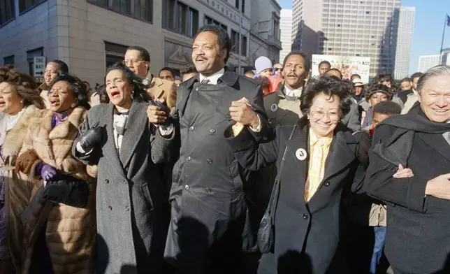 FILE - Coretta Scott King holds hands while singing with the Rev. Jesse Jackson and Christine Farris, the sister of Dr. Martin Luther King, Jr., as they parade on Peachtree Street in Atlanta on Monday, Jan. 19, 1987 to honor King's birthday. At left in Mrs. Alveda king Beall and at right is Lupita Aquino Kashiwahara. (AP Photo/Charles Kelly, File)
