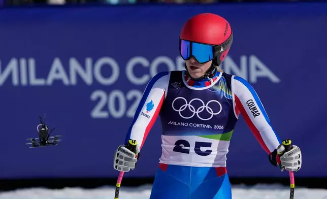 A drone is seen in front of France's Camille Cerutti at the finish area of an alpine ski women's downhill race, at the 2026 Winter Olympics, in Cortina d'Ampezzo, Italy, Sunday, Feb. 8, 2026. (AP Photo/Andy Wong)
