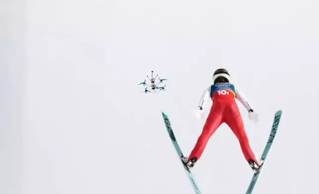 A drone follows Lisa Eder, of Austria, soaring through the air during the ski jumping mixed team competition at the 2026 Winter Olympics, in Predazzo, Italy, Tuesday, Feb. 10, 2026. (AP Photo/Evgeniy Maloletka)