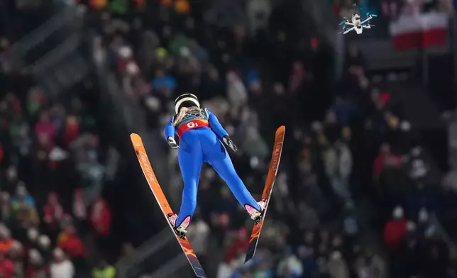 A drone follows Heta Hirvonen, of Finland, soaring through the air during the ski jumping mixed team competition at the 2026 Winter Olympics, in Predazzo, Italy, Tuesday, Feb. 10, 2026. (AP Photo/Evgeniy Maloletka)