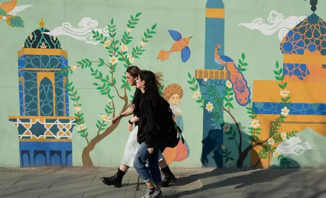 Women walk past an Islamic-themed painting on a wall at Enqelab-e-Eslami, or Islamic Revolution, street in downtown Tehran, Iran, Wednesday, Feb. 25, 2026. (AP Photo/Vahid Salemi)
