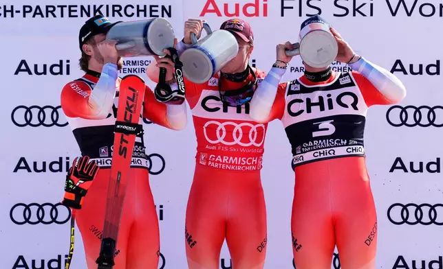 Switzerland's Marco Odermatt, center, winner of a men's World Cup downhill race, on the podium with second placed Switzerland's Alexis Monney, left, and third placed Switzerland's Stefan Rogentin, in Garmisch Partenkirchen , Germany, Saturday, Feb. 28, 2026. (AP Photo/Giovanni Auletta)