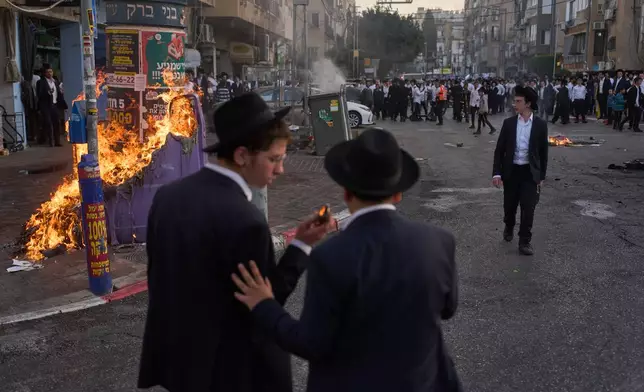 Ultra-Orthodox Jewish men burn trash during clashes with police after two female Israeli soldiers were rescued from riots that erupted during a welfare visit in Bnei Brak, Sunday, Feb. 15, 2026. (AP Photo/Oded Balilty)