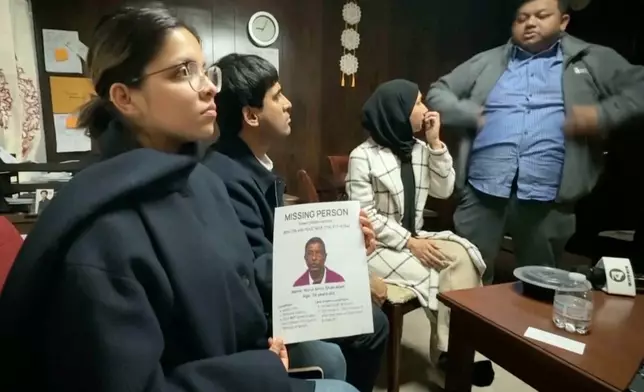 This image made from video provided by WKBW.COM shows a family friend holding a missing person flyer for Nurul Amin Shah Alam, while sitting with other family friends including Khaleda Shah, second from right, and MD Karim, far right, on Wednesday, Feb. 25, 2026, in Buffalo, N.Y. (WKBW.COM via AP)