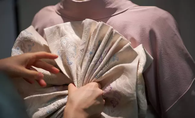 Nao Shimizu, Representative Director of Kimono Sunao Co., Ltd., left, demonstrates various ways of tying an obi on assistant Emiko Terai during a kimono presentation in Tokyo Tuesday, Nov. 11, 2025. (AP Photo/Eugene Hoshiko)