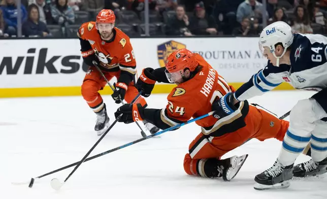 Anaheim Ducks center Jansen Harkins, center, and Winnipeg Jets defenseman Logan Stanley, right, vie for the puck during the first period of an NHL hockey game, Friday, Feb. 27, 2026, in Anaheim, Calif. (AP Photo/Kyusung Gong)