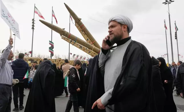 A cleric talks on his phone as he walks in front of domestically-built missiles during an annual rally marking 1979 Islamic Revolution at the Azadi, or Freedom, square in Tehran, Iran, Wednesday, Feb. 11, 2026. (AP Photo/Vahid Salemi)