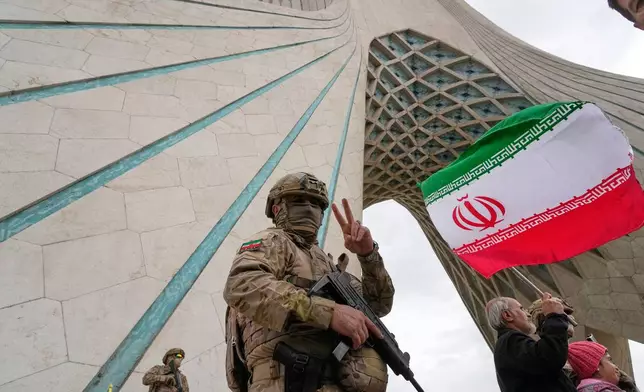 A member of the Revolutionary Guard flashes a victory sign while taking position as a man holds an Iranian flag under the Azadi, or freedom, monument tower during an annual rally marking 1979 Islamic Revolution at the Azadi square in Tehran, Iran, Wednesday, Feb. 11, 2026. (AP Photo/Vahid Salemi)