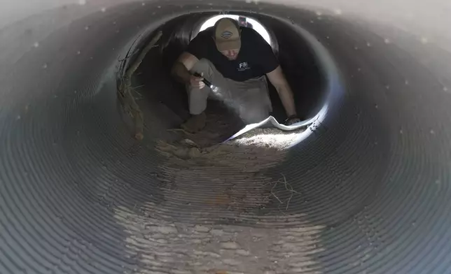 An investigator looks inside a culvert in the neighborhood where Annie Guthrie, whose mother Nancy Guthrie has been missing for more than a week, lives just outside Tucson, Ariz., on Tuesday, Feb. 10, 2026. (AP Photo/Ty ONeil)