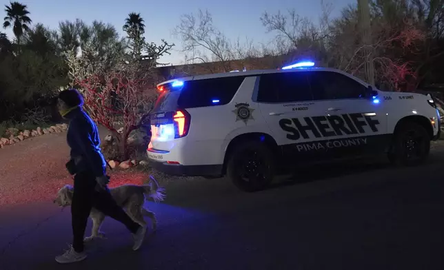 A woman walks her dog past a Pima county sheriff's vehicle parked in front of Nancy Guthrie's home on Tuesday, Feb. 10, 2026 in Tucson, Ariz. (AP Photo/Ty ONeil)