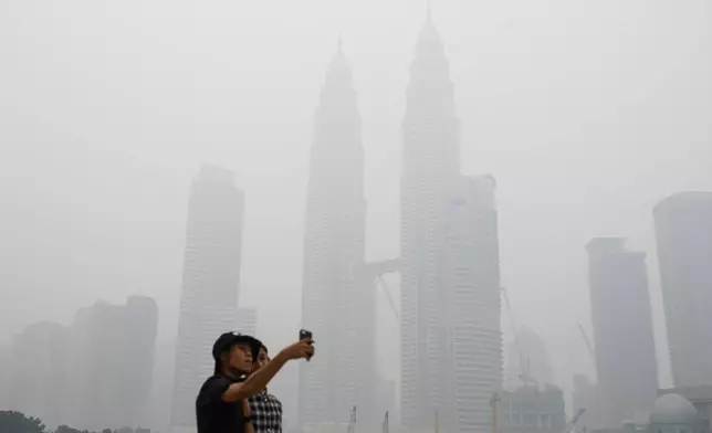 FILE -Tourists take a selfie against Malaysia's landmark building Petronas Twin Towers shrouded with haze in Kuala Lumpur, Malaysia on Sept. 26, 2015. (AP Photo/Joshua Paul, File)