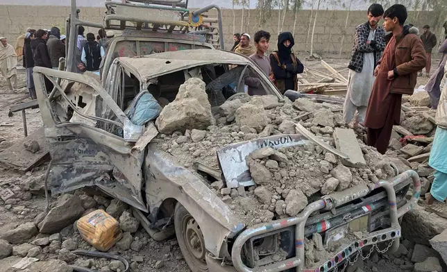 Local residents stand next to a damaged car at the site of a cross-border Pakistani army strike in the Behsud district of Nangarhar province, Afghanistan, Sunday, Feb. 22, 2026. (AP Photo/Hedayat Shah)