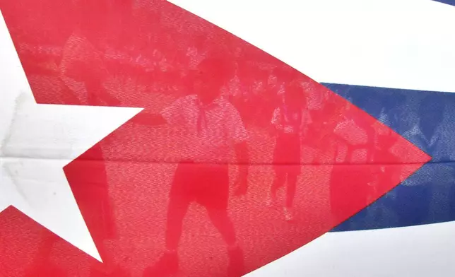 FILE - Children are seen through the Cuban flag while they walk to the Havana's Malecon to toss flowers into the ocean in commemoration of the anniversary of the death of the Cuban revolutionary Commander Camilo Cienfuegos, Thursday, Oct. 28, 2004 in Havana, Cuba. (AP Photo/Cristobal Herrera, File)