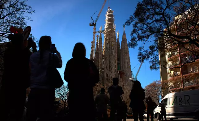 People watch as a crane lifts the upper arm of the cross onto the Tower of Jesus Christ at the Sagrada Familia in Barcelona, Spain, Friday, Feb. 20, 2026, reaching the basilica's maximum height of 172.5 meters (566 feet). (AP Photo/Emilio Morenatti)