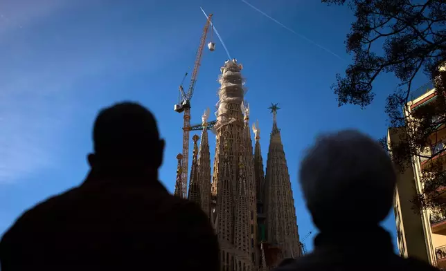 People watch as a crane lifts the upper arm of the cross onto the Tower of Jesus Christ at the Sagrada Familia in Barcelona, Spain, Friday, Feb. 20, 2026, reaching the basilica's maximum height of 172.5 meters (566 feet). (AP Photo/Emilio Morenatti)