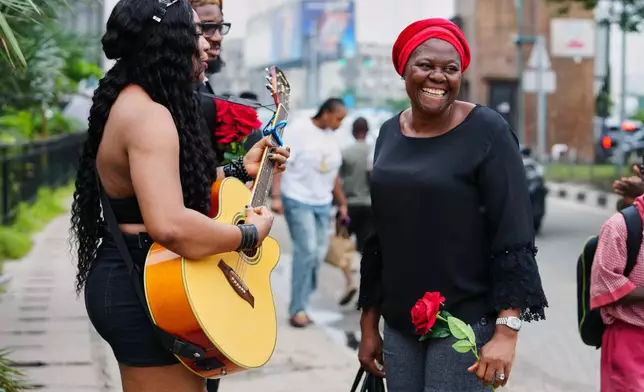 A commuter, right reacts as Nigerian rock musician Bianca "Clayrocksu" Okorocha, left, accompanied by Daniel Onyemachi-Chiweolu, popularly known as Machigold, behind, sings love songs handing single-stem roses to commuters ahead of Valentine's Day in Lagos, Nigeria, Tuesday, Feb.10, 2026. (AP Photo/Sunday Alamba)