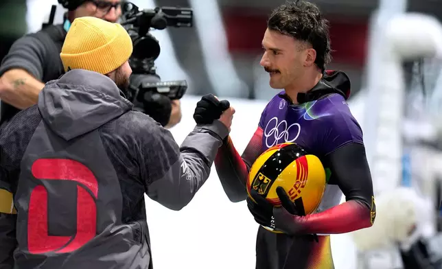 Germany's Axel Jungk, right, arrives at the finish during a men's skeleton run at the 2026 Winter Olympics, in Cortina d'Ampezzo, Italy, Thursday, Feb. 12, 2026. (AP Photo/Alessandra Tarantino)