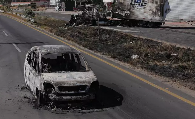 FILE - Seen through a charred vehicle, other burned vehicles litter the road after the Mexican army killed the leader of the Jalisco New Generation Cartel, Nemesio Oseguera Cervantes, known as "El Mencho," in Guadalajara, Mexico, Feb. 23, 2026. (AP Photo/Marco Ugarte, File)