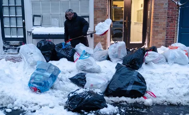 Key Lim, 55, of Quincy, removes snow from a sidewalk lined with trash bags in front of the laundromat that he manages on Tuesday, Feb. 24, 2026, in Boston. (AP Photo/Sophie Park)