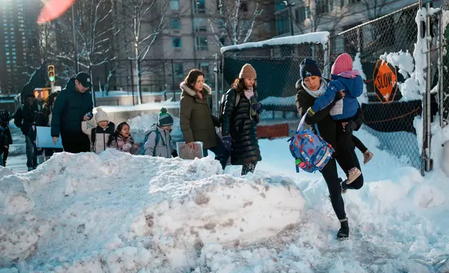 A woman carries a child over piles of plowed snow as she walks a girl to school, Tuesday, Feb. 24, 2026, in New York. (AP Photo/Eduardo Munoz Alvarez)