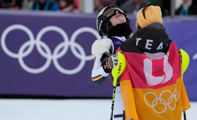 Germany's Emma Aicher, left, is hugged by teammate Germany's Kira Weidle Winkelmann at the finish area of an alpine ski, women's team combined race, at the 2026 Winter Olympics, in Cortina d'Ampezzo, Italy, Tuesday, Feb. 10, 2026. (AP Photo/Andy Wong)
