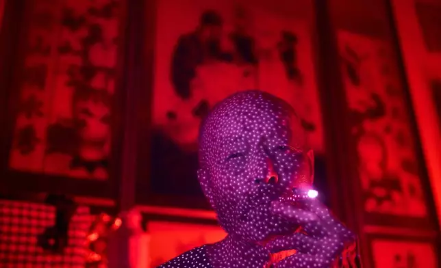 FILE - Yang Guoliang, who has been under surveillance by Chinese officials after complaining about a land dispute to the central government in Beijing, is illuminated by cellphone infrared facial recognition beams as he smokes a cigarette inside his home in Changzhou, in eastern China's Jiangsu Province, Sept. 7, 2025. (AP Photo/Ng Han Guan, File)