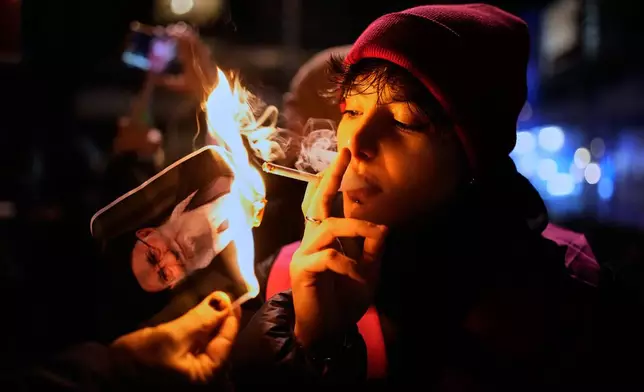 FILE - A protester smokes a cigarette after lighting it off a burning poster of Iran's Supreme Leader Ayatollah Ali Khamenei in Berlin, Germany, Jan. 14, 2026, in support of the nationwide mass protests in Iran against the government. (AP Photo/Ebrahim Noroozi, File)