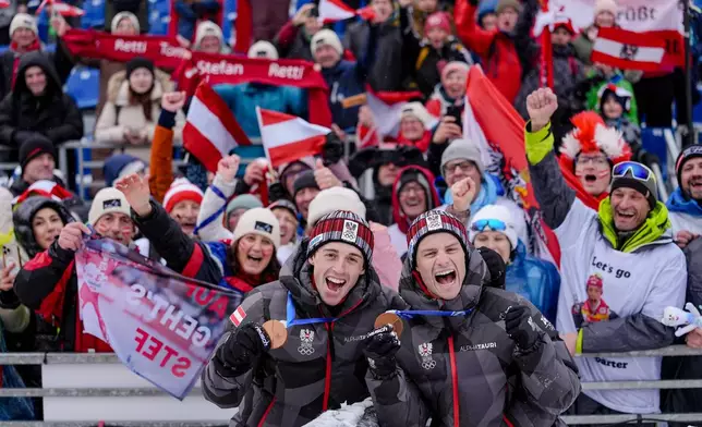 Stefan Rettenegger, left, and Johannes Lamparter, of Austria, pose with supporters after winning the bronze medal in the nordic combined team sprint at the 2026 Winter Olympics, in Tesero, Italy, Thursday, Feb. 19, 2026. (AP Photo/Matthias Schrader)