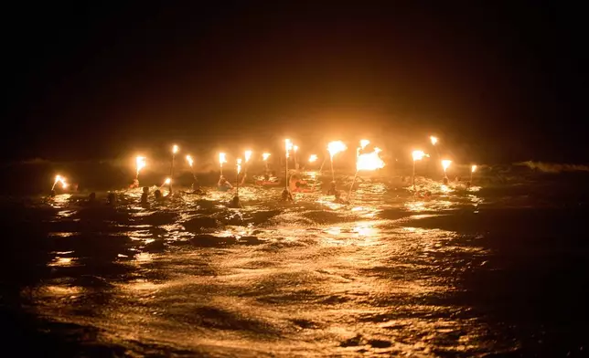 Lifeguards holding torches, wade into the Atlantic ocean in a ceremony to commemorate Lifeguard Day, to honor their commitment to safety and aquatic rescue, in Mar Azul, Argentina, Saturday, Feb. 14, 2026. (AP Photo/Rodrigo Abd)