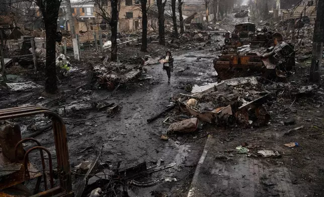 FILE - A woman navigates a debris-filled street where destroyed Russian military vehicles stand in Bucha on the outskirts of Kyiv, Ukraine, Sunday, April 3, 2022. (AP Photo/Rodrigo Abd, File)