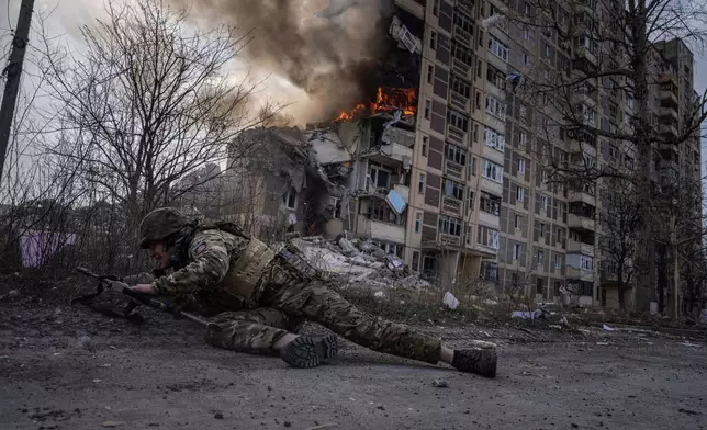 FILE - A Ukrainian police officer takes cover in front of a burning building that was hit in a Russian airstrike in Avdiivka, Ukraine, Friday, March 17, 2023. (AP Photo/Evgeniy Maloletka, File)