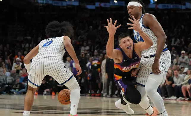 Phoenix Suns guard Grayson Allen reacts after loosing the ball in between Orlando Magic guard Anthony Black (0) and center Wendell Carter Jr. during the second half of an NBA basketball game, Saturday, Feb. 21, 2026, in Phoenix. (AP Photo/Rick Scuteri)
