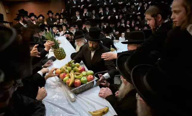 Ultra-Orthodox Jews from the Nadvorna Hasidic dynasty pass a platter of fruit during celebrations marking the Jewish holiday of Tu Bishvat, the "New Year of the Trees," in the ultra-Orthodox town of Bnei Brak, Israel, Monday, Feb. 2, 2026. (AP Photo/Oded Balilty)