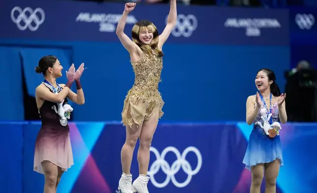 From left to right, silver medalist Kaori Sakamoto of Japan, gold medalist Alysa Liu of the United States, and bronze medalist Ami Nakai of Japan, jump on the podium to receive their medals after competing in the women's free skate program in figure skating at the 2026 Winter Olympics, in Milan, Italy, Thursday, Feb. 19, 2026. (AP Photo/Natacha Pisarenko)