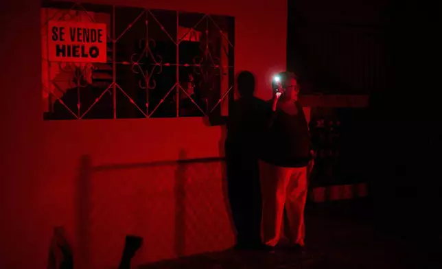 FILE - A woman holds up a cell phone flashlight as she chats with a friend during a scheduled power outage as part of energy rationing in Santa Cruz del Norte, home to one of Cuba's largest thermoelectric plants, Feb. 3, 2026. (AP Photo/Ramon Espinosa, File)