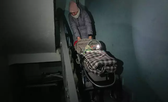 FILE - Yuliia Dolotova pulls her son in a stroller up apartment stairs during a power outage caused by Russia's repeated air strikes on the country's power grid, in Kyiv, Ukraine, Feb. 2, 2026. (AP Photo/Sergey Grits, File)