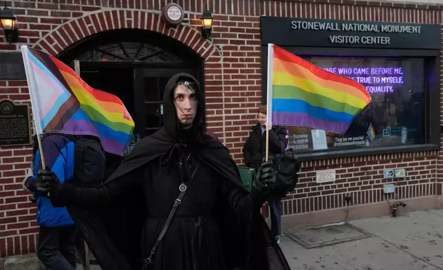 A protestor stands outside the Stonewall Inn National Monument Visitor Center after New York politicians and activists raised a rainbow flag on a pole in Christopher Park across the street, Thursday, Feb. 12, 2026, in New York, a few days after it was removed by the National Park Service to comply with guidance from the Trump administration. (AP Photo/Yuki Iwamura)