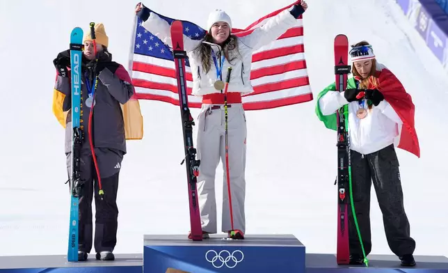 United States' Breezy Johnson, center, gold medal in an alpine ski women's downhill race, celebrates on the podium with silver medalist Germany's Emma Aicher, left, and bronze medalist Italy's Sofia Goggia, at the 2026 Winter Olympics, in Cortina d'Ampezzo, Italy, Sunday, Feb. 8, 2026. (AP Photo/Andy Wong)