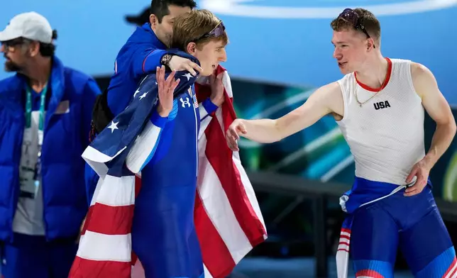 U.S. team members drape gold medallist Jordan Stolz in the national flag for his victory lap after the men's 500 meters speedskating race at the 2026 Winter Olympics, in Milan, Italy, Saturday, Feb. 14, 2026. (AP Photo/Luca Bruno)