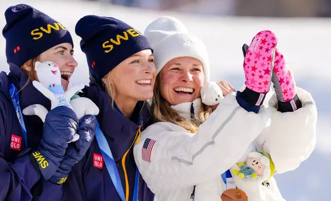 Silver medalist Ebba Andersson, of Sweden, from left, gold medalist Frida Karlsson, of Sweden, and bronze medalist Jessie Diggins, of the United States, pose for a selfie on the podium of the cross country skiing women's 10km interval start free at the 2026 Winter Olympics, in Tesero, Italy, Thursday, Feb. 12, 2026. (AP Photo/Kirsty Wigglesworth)