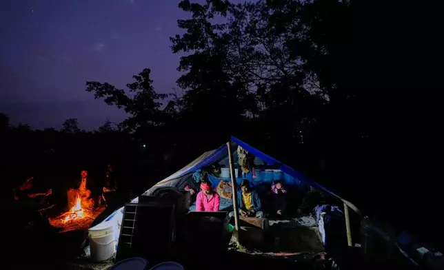 A migratory beekeeper prepares dinner in a makeshift tent as others relax after work at a bee colony near a mustard field in the Binnabari village in Baksa district of Assam, India, Thursday, Jan. 15, 2026. (AP Photo/Anupam Nath)