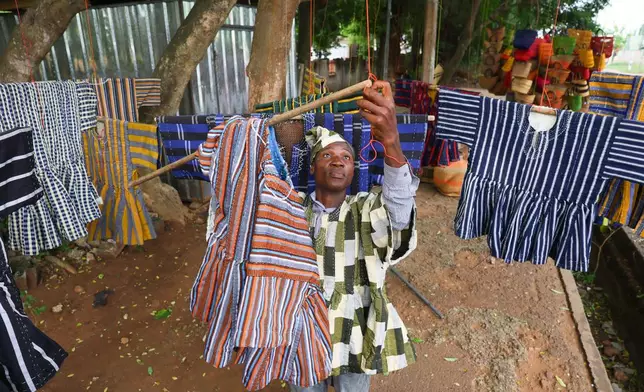 Clement Azaabire hangs traditional fugu garments under a tree on display for sale along a street in Accra, Ghana, Wednesday, Feb. 18, 2026. (AP Photo/Tsraha Yaw)