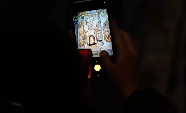 A man takes a picture at a restored fresco to the memory of late Italy's King Umberto II depicting Angels inside the Basilica of St. Lawrence in Lucina in Rome, Sunday, Feb. 1, 2026. (AP Photo/Gregorio Borgia)